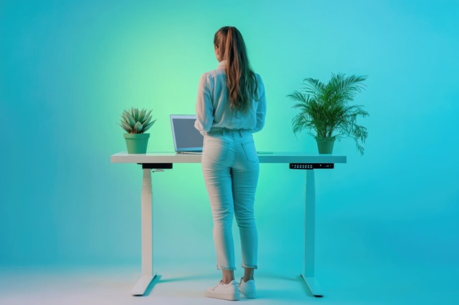 Osoba stoi przy biurku z roślinami, które podtrzymuje solidny stelaż biurka.